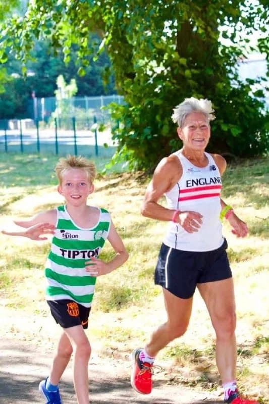 Penny Barber running in an England Masters vest alongside a young Tipton Harriers athlete